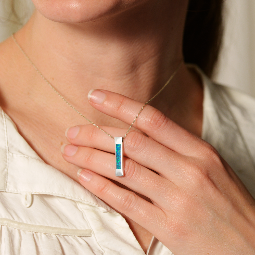 Opals & Ashes Bar Unisex Memorial Pendant Silver. Modelled on female. Ashes blended with Pacific Blue Opals. Held in fingers.